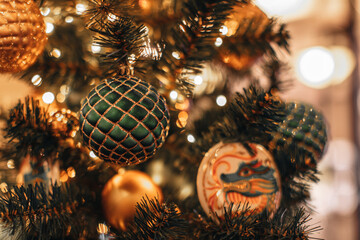 Festive golden green shiny Christmas ball with a dragon pattern hanging on a Christmas tree with...