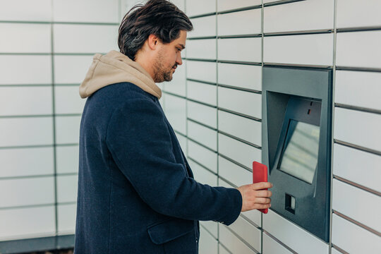Man scanning QR code with smart phone on parcel locker machine