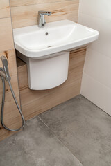 Wall mounted white porcelain sink with silver sensor faucet in modern bathroom with concrete and...