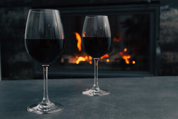 Two glasses of red wine on a background of a burning fireplace. Cozy atmosphere winter evening.