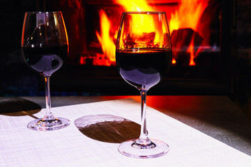 Two glasses of red wine on a background of a burning fireplace. Cozy atmosphere winter evening.