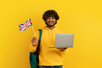 Happy young indian guy holding laptop and flag of UK - obrazy, fototapety, plakaty