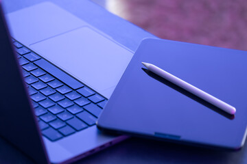 Digital tablet, stylus pen and laptop on the desktop, close up.