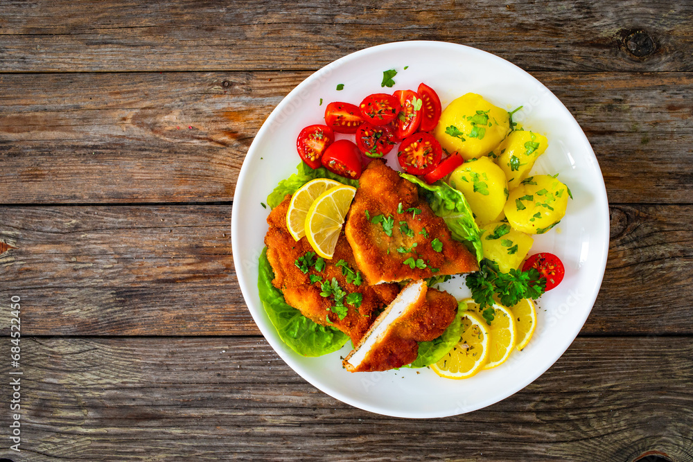 Poster Crispy breaded fried chicken cutlet with fresh vegetables and boiled potatoes on wooden table
