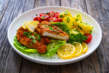 Crispy breaded fried chicken cutlet with fresh vegetables and boiled potatoes on wooden table
