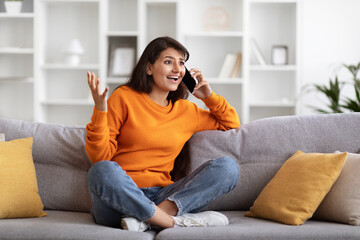 Emotional pretty young indian woman talking on phone at home