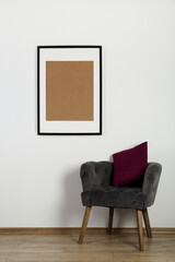 Comfortable armchair, cushion and picture frame on wall indoors. Interior element