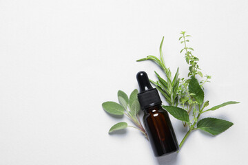 Bottle of essential oil, different herbs and flowers on white background, flat lay. Space for text