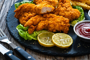 Fried breaded chicken nuggets served with French fries and vegetables on wooden table
