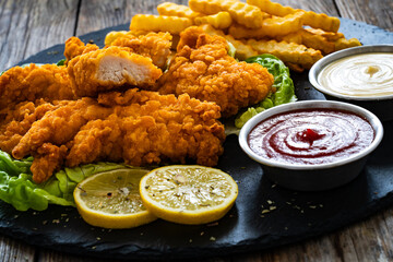 Fried breaded chicken nuggets served with French fries and vegetables on wooden table
