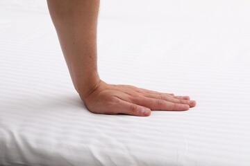 Man touching soft mattress with bed sheet, closeup