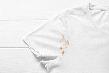 Stylish t-shirt with stain on white wooden table, top view