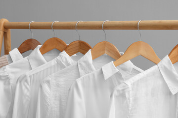 Rack with different stylish shirts on wooden hangers against grey wall, closeup. Organizing clothes - Powered by Adobe