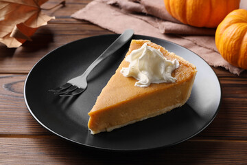 Piece of delicious pumpkin pie with whipped cream and fork on wooden table, closeup