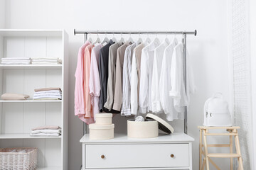 Wardrobe organization. Rack with different stylish clothes, chest of drawers and shelving unit near white wall indoors