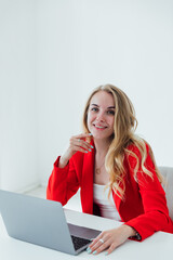 Attractive cheerful business woman in red shirt working on laptop at modern office