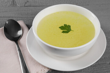 Tasty broth in bowl on grey wooden table, closeup