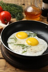 Frying pan with tasty cooked eggs, dill and other products on wooden table, closeup