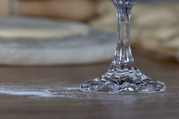Fokus auf Fuß eines Kristallglases auf einem Tisch mit Mehl, Wareniki, Holzbrett, Nudelholz 