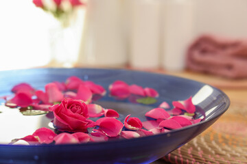 Obraz na płótnie Canvas Pink roses and petals in bowl with water on table, closeup