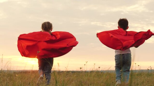 Kids donning superhero capes frolic and run across open field at evening sunset