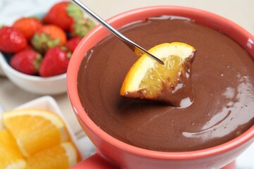 Dipping fresh orange into fondue pot with melted chocolate at table, closeup