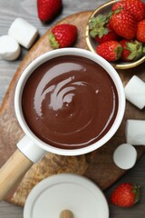 Fondue pot with melted chocolate, sweet marshmallows and strawberries on wooden table, flat lay