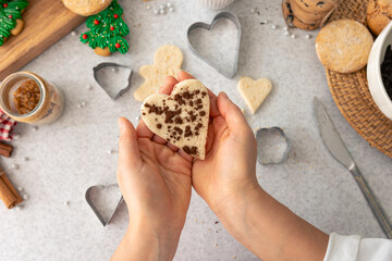 Shape of gingerbread heart from dough in female hands in the kitchen.