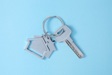 Key with keychain in shape of house on light blue background, top view