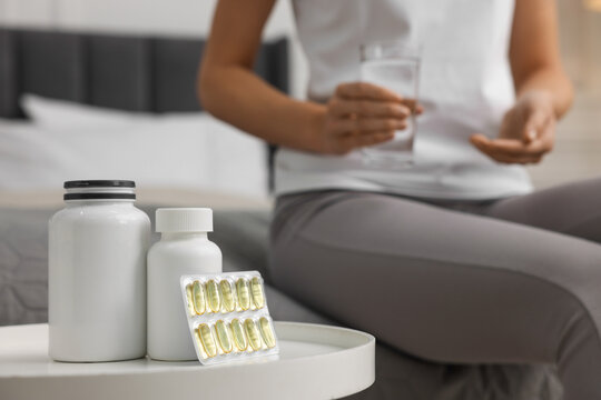 Woman holding glass of water, focus on table with pills in room. Weight loss