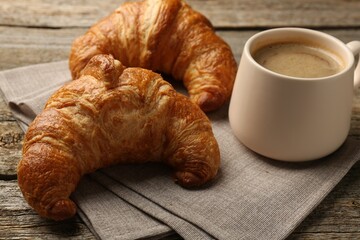 Delicious fresh croissants and cup of coffee on table, closeup