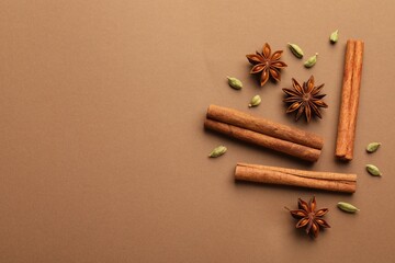Cinnamon sticks, star anise and cardamom pods on brown background, flat lay. Space for text