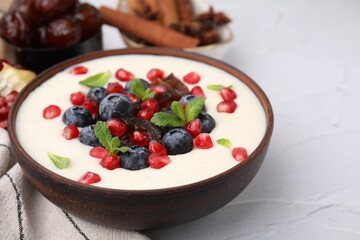 Delicious semolina pudding with blueberries, pomegranate, dates and mint in bowl on white table, closeup. Space for text