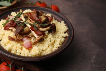Tasty couscous with mushrooms and bacon in bowl on brown table, closeup. Space for text
