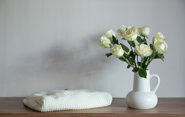 knitted clothing and white roses in jug on modern dresser