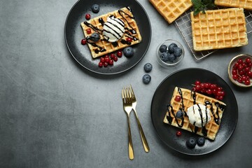 Delicious Belgian waffles with ice cream, berries and chocolate sauce on grey textured table, flat lay. Space for text