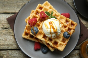 Delicious Belgian waffles with ice cream, berries and caramel sauce on wooden table, top view