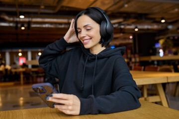 European brunette woman in a hoodie listens to music on headphones while sitting in a cafe