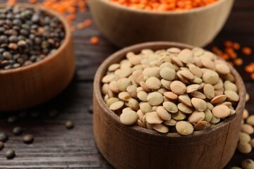 Raw lentils in bowls on wooden table, closeup