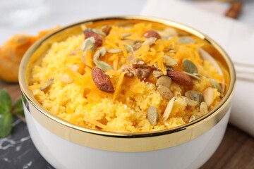 Tasty cornmeal with nuts, pumpkin and seeds in bowl on table, closeup