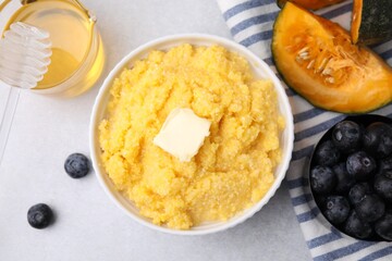 Tasty cornmeal with butter in bowl and products on light gray table, flat lay