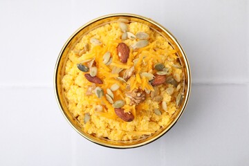 Tasty cornmeal with nuts, pumpkin and seeds in bowl on white tiled table, top view