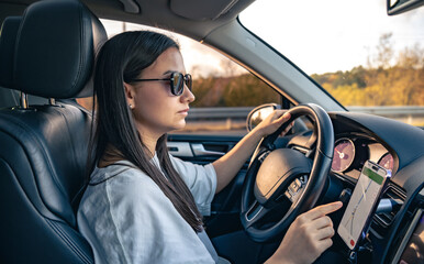 An attractive young woman driving a car uses a navigator.
