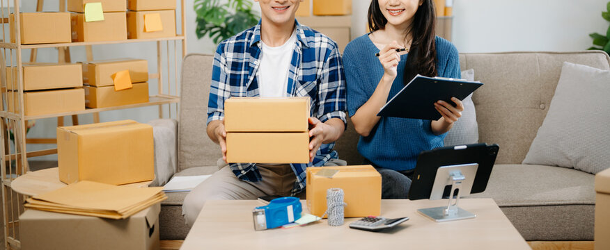 Startup small business SME, Entrepreneur owner man and woman using smartphone or tablet taking receive and checking online purchase shopping order to preparing pack product box. on sofa .