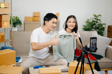 Two Asian blogger showing clothes in front of the camera to recording vlog video live streaming at her shop. Online Shopping Cart notion.
