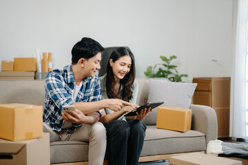 Young attractive couple man and woman use tablet and smartphone online shopping furniture decorate house with carton package move in new house. ฃ.