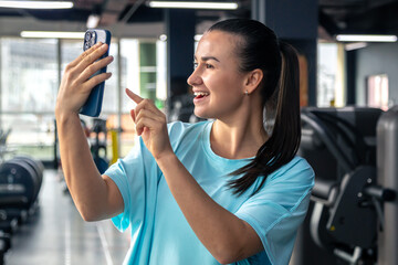 Young woman in the gym with a smartphone takes a selfie.
