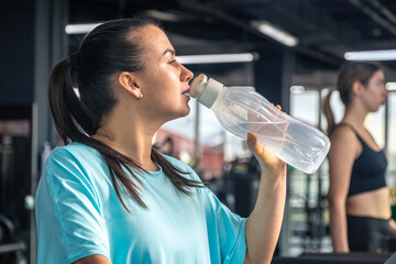 Woman drinking water after exercising on treadmill in gym.