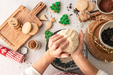 Hands knead dough on a table, decorated with festive decorations for Christmas.