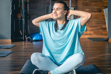 Young woman sitting on a mat in a fitness center, doing yoga and stretching.